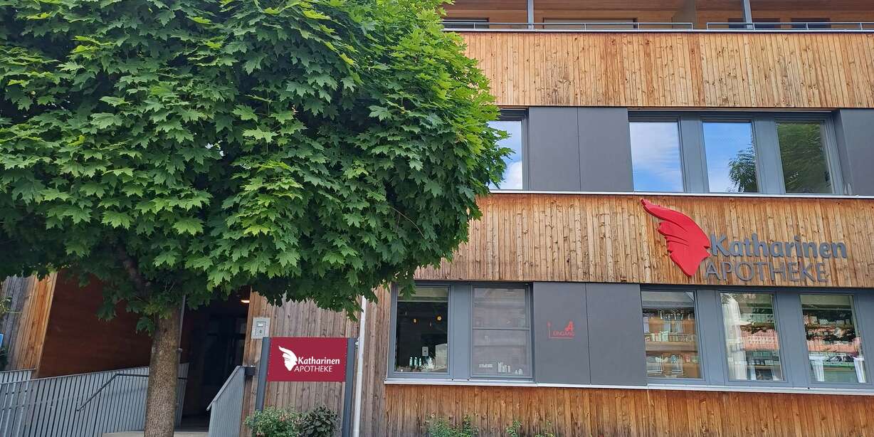 Moderne Apotheke mit großer Glasfassade, roten Akzenten, Leuchtschrift und einladendem Eingangsbereich.