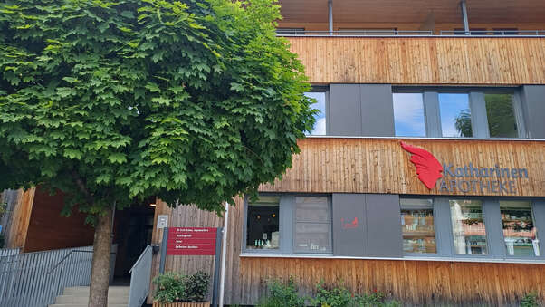 Moderne Apotheke mit großer Glasfassade, roten Akzenten, Leuchtschrift und einladendem Eingangsbereich.